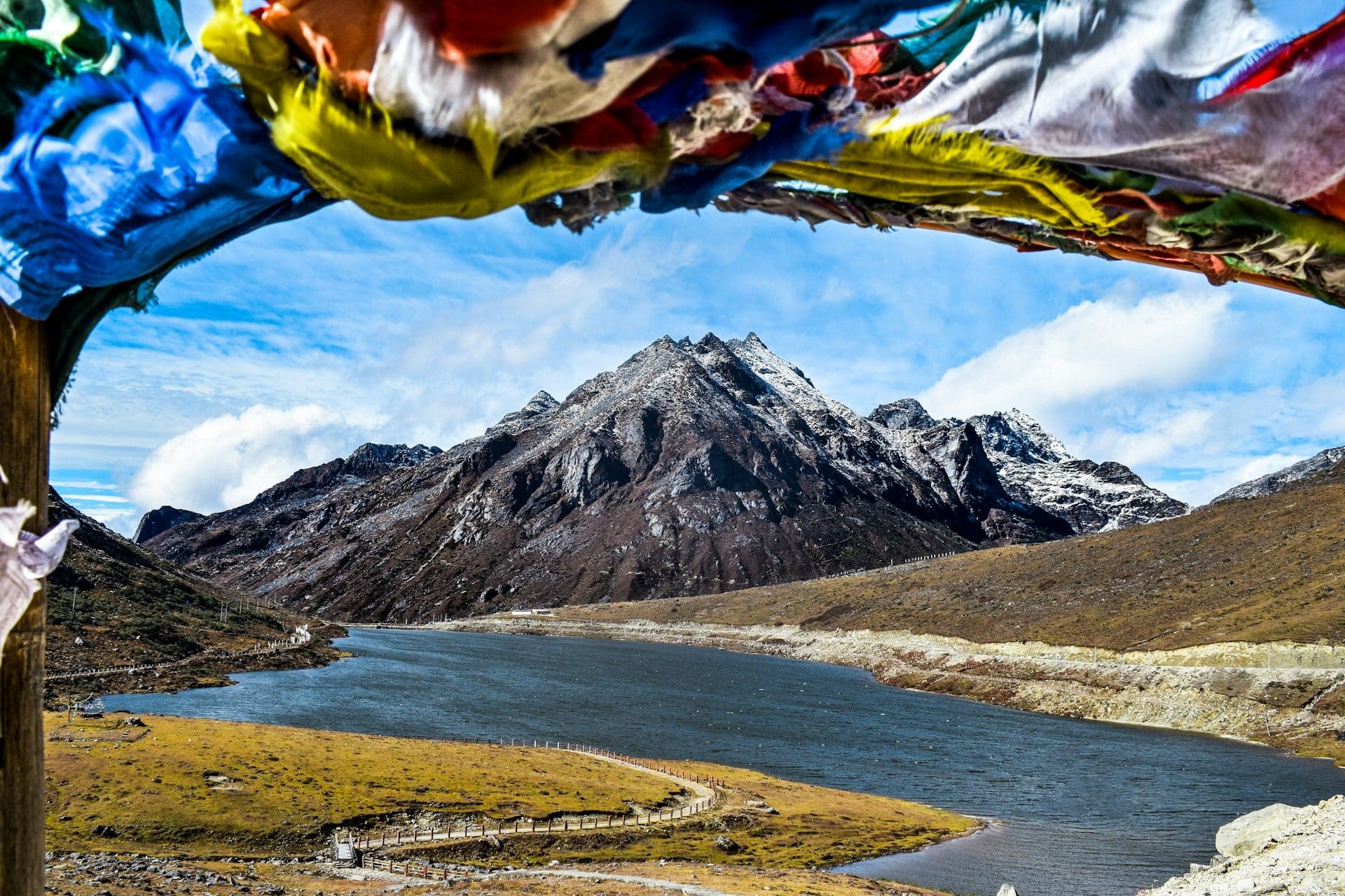 Prayer flags framing a high-altitude lake and snow-dusted peak near Sela Pass, Arunachal Pradesh