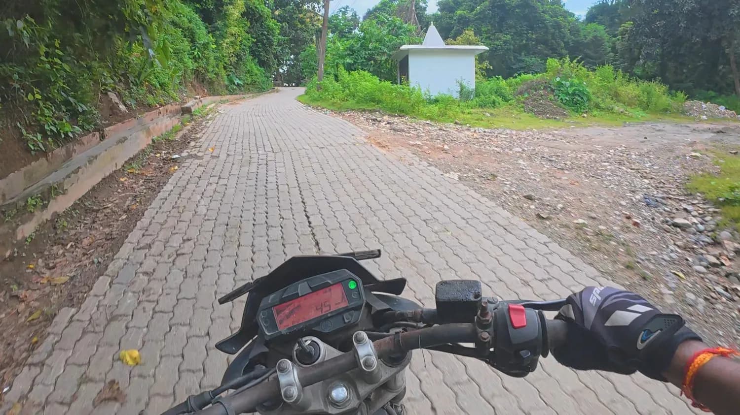 Riding our Yamaha FZ rental bike with gloves on a paved hill road past a small roadside shrine