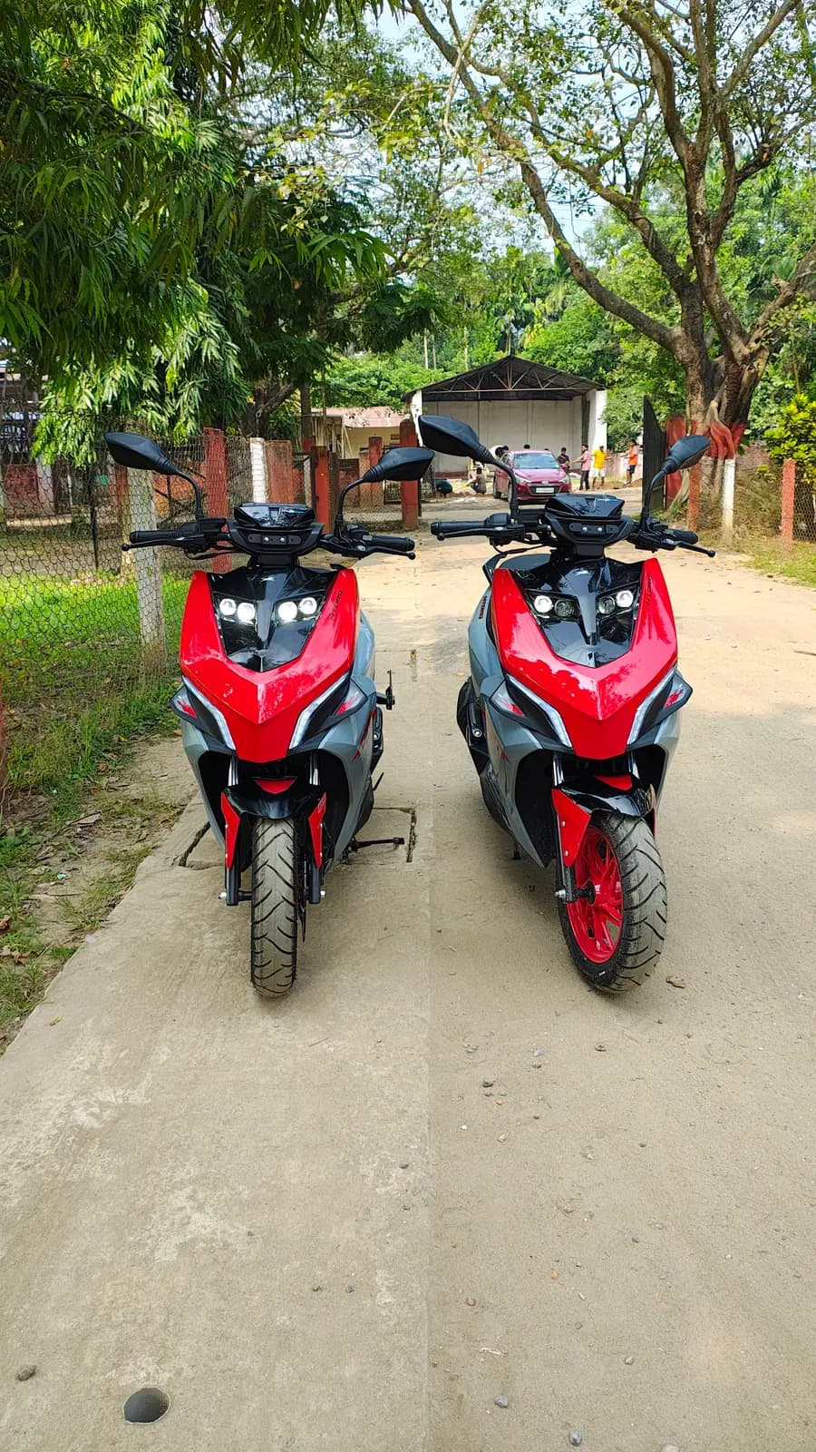 Two of our TVS NTorq 150 rental scooters in red and grey, parked side by side on a tree-lined lane