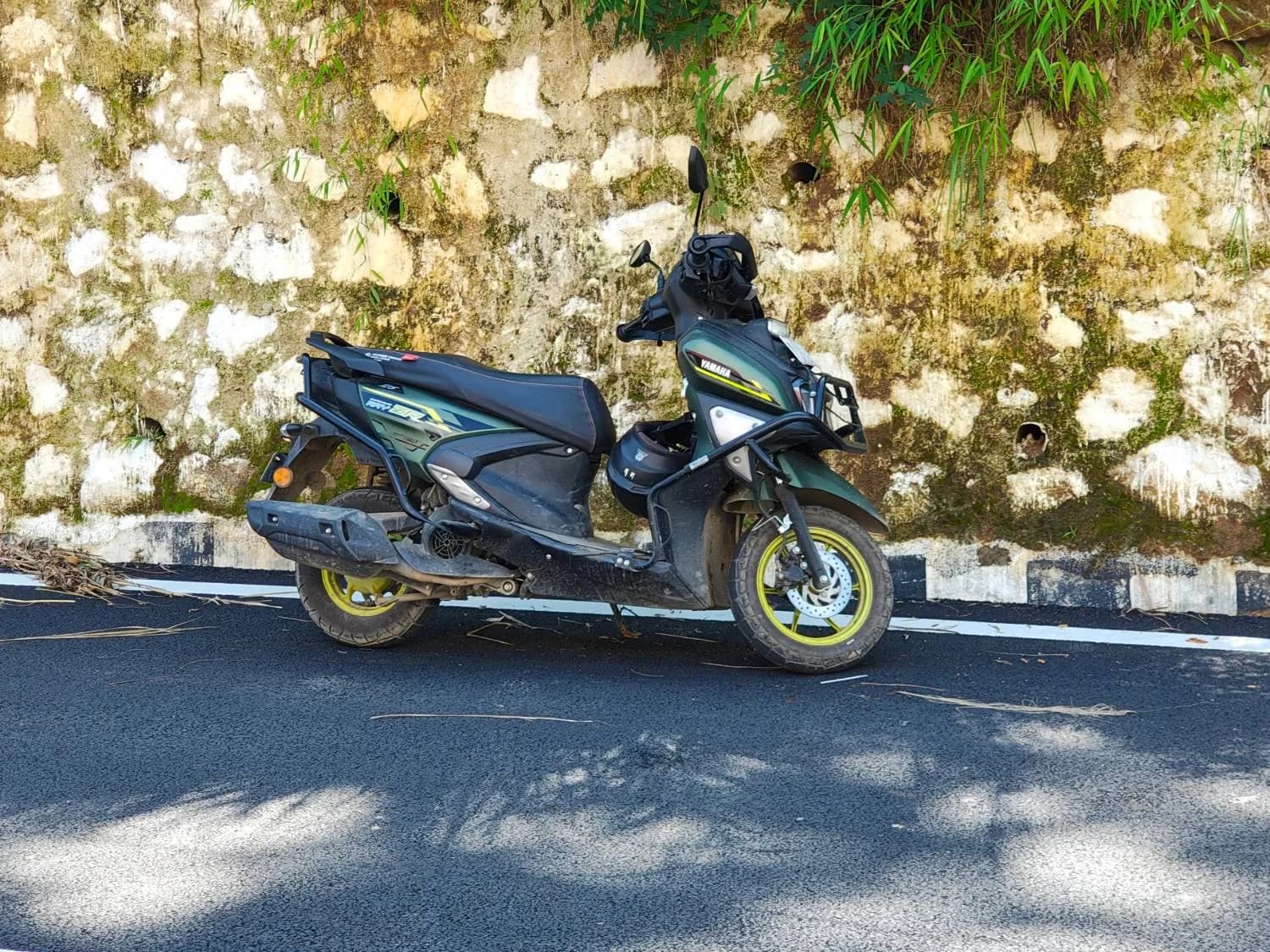 Our Yamaha RayZR 125 rental scooter, fitted with crash guards and carrying a helmet, parked on a hill road
